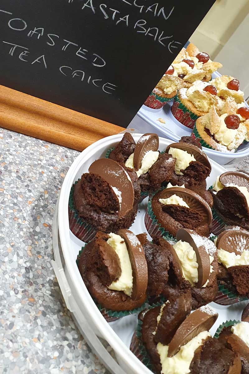 A picture with two plates of cakes. One has chocolate cupcakes with cream inside. The other is further back and has mini sponge cakes with cream and a strawberry on top.