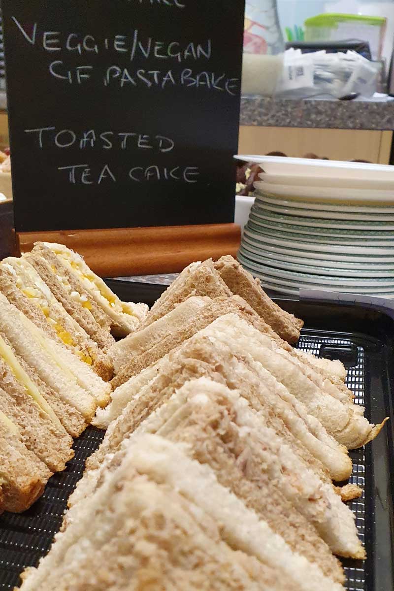 A platter of sandwiches on a black plastic tray. There is a mini chalkboard behind it saying what is on the menu.