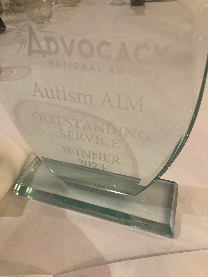 A glass trophy that says, in white text on the front, "National Advocacy Awards" "Autism AIM" "Outstanding Service Winner 2023"