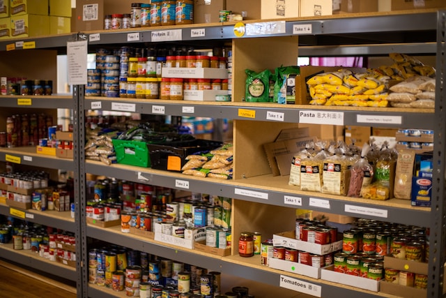 A photo of wooden shelves inside a food bank. They are stacked with tins, jars and bags of food.