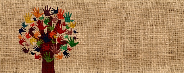 An image of a tree shape with leaves and branches made up of coloured hand prints, on a woven brown fabric background.