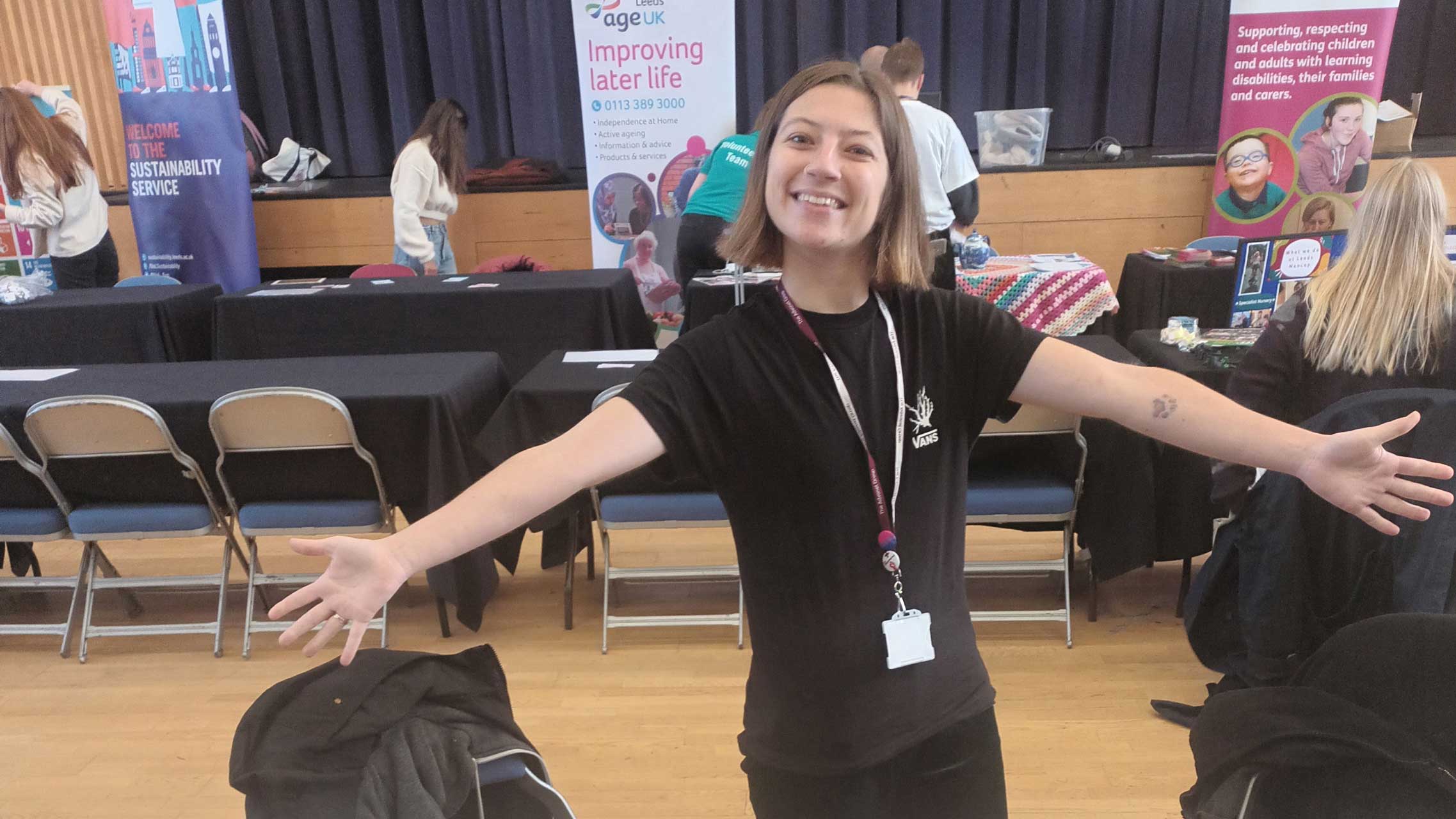 Beth, our Volunteer Coordinator, with her arms outstretched while in front of a stall at an event.