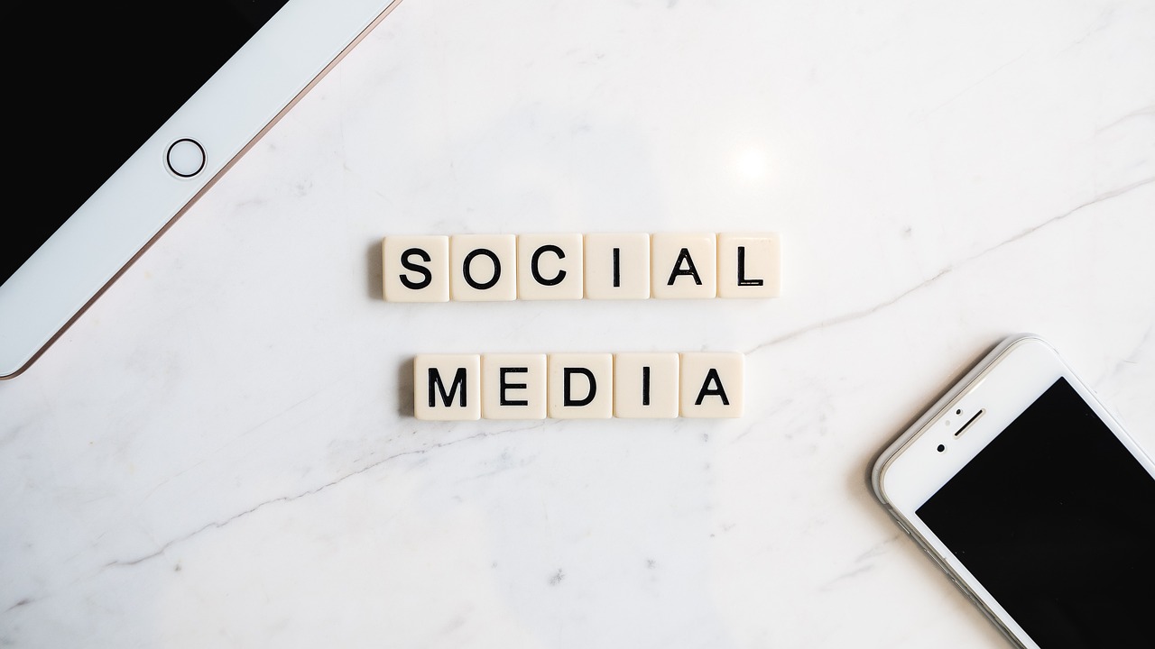 An image of some small Scrabble tiles with letters spelling out the words "Social Media", laid out on a white table. There is also a tablet and smartphone on the table.