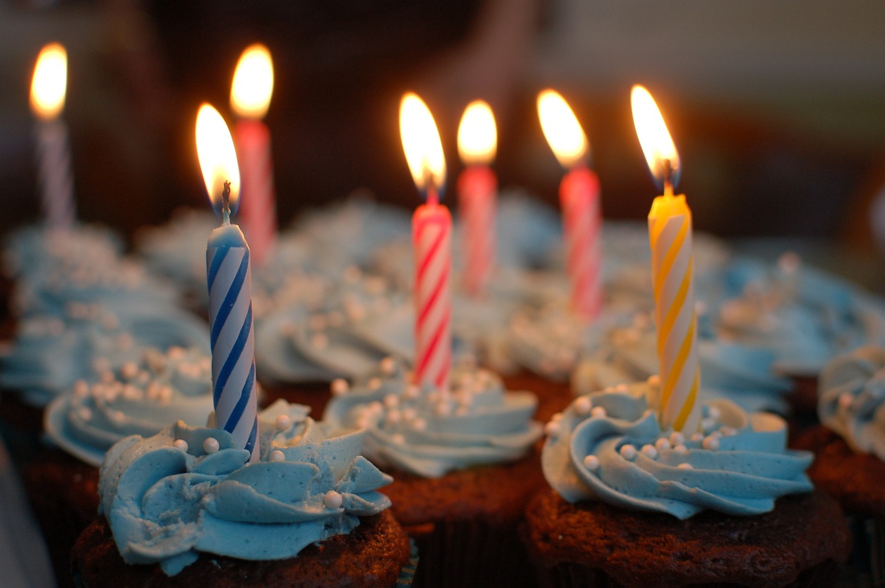 A picture of some cupcakes covered in frosting, each with a lit birthday cake candle in the middle.