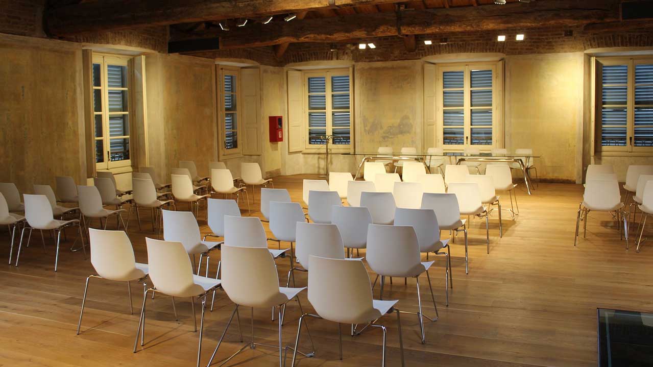 An image of a room with several rows of white chairs laid out, in preparation for an in-person training session.