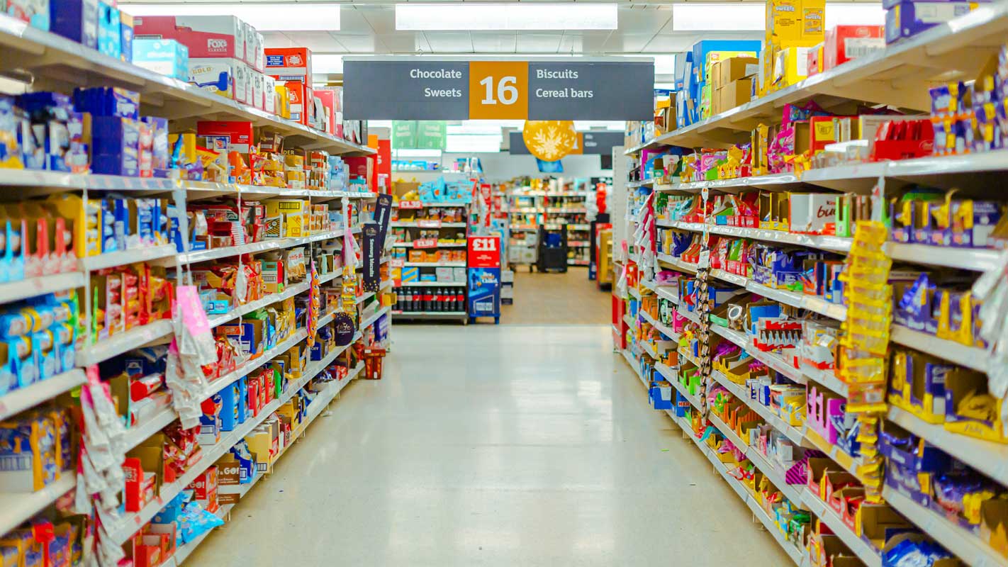 An aisle inside a Sainsbury's Supermarket, with shelves full of food either side of it.